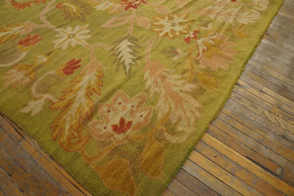 Low-pile olive green rug featuring a large-scale floral pattern in blush, terracotta, and gold on wood flooring.