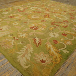 Olive green rug with gold, rust, and pink stylized floral patterns covers light wood flooring.