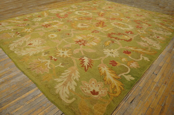 Olive green rug with gold, rust, and pink stylized floral patterns covers light wood flooring.