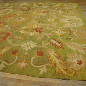 Green rug with large gold, rust, and pink floral patterns on distressed wood flooring.