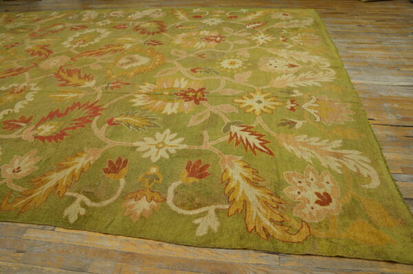 Green rug with large gold, rust, and pink floral patterns on distressed wood flooring.