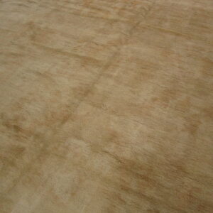 A plush, solid light brown area rug displays subtle tonal variation on warm brown wood plank flooring.