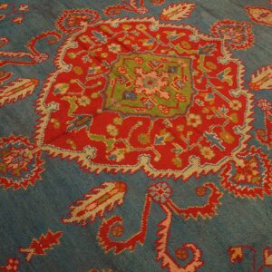 Teal blue rug featuring a central red medallion with green, yellow, and pink traditional patterns.