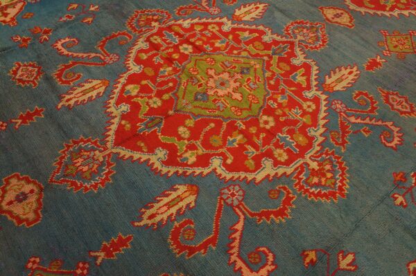 Teal blue rug featuring a central red medallion with green, yellow, and pink traditional patterns.