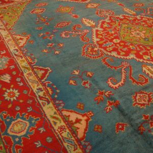 Ornate teal rug with large red motifs and borders rests on light-colored wooden plank flooring.