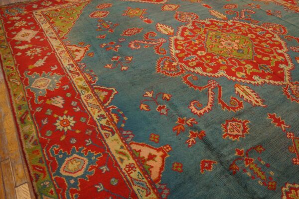 Ornate teal rug with large red motifs and borders rests on light-colored wooden plank flooring.