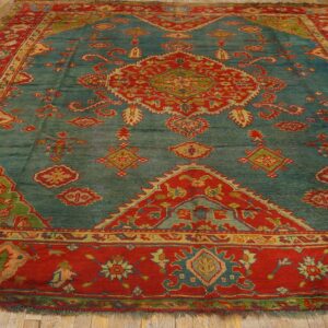 Teal rug with a detailed red, green, and gold medallion and thick red borders on wooden flooring.