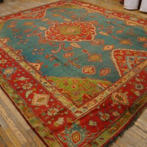 Teal and red traditional rug with intricate floral and geometric patterns laid on distressed wood plank flooring.