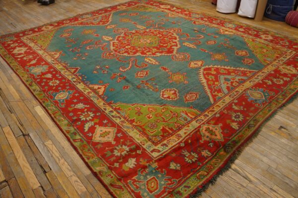 Teal and red traditional rug with intricate floral and geometric patterns laid on distressed wood plank flooring.