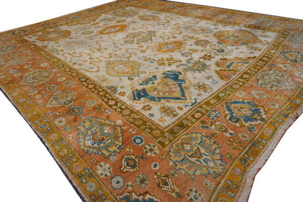 Ornate patterned rug featuring a rust border surrounding an off-white center with blue and gold motifs.