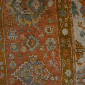 High-pile rug texture with complex traditional patterns in rust orange, cream, moss green, and gold.