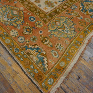 Rust and teal geometric rug with a mustard yellow border rests on distressed wooden plank flooring.