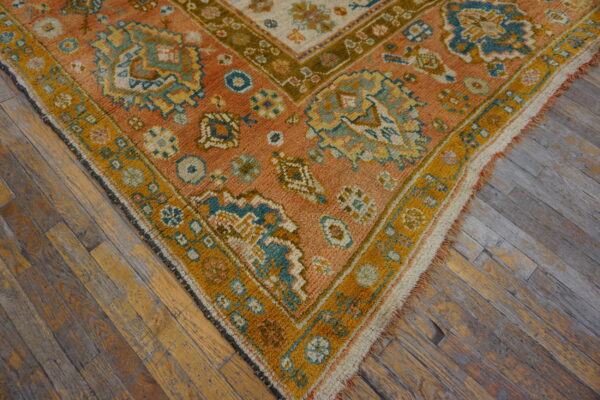 Rust and teal geometric rug with a mustard yellow border rests on distressed wooden plank flooring.