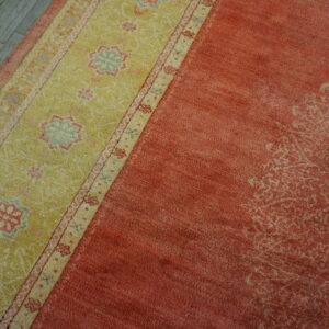Rust-colored rug with a wide lime-green border featuring floral medallions rests on distressed plank flooring.