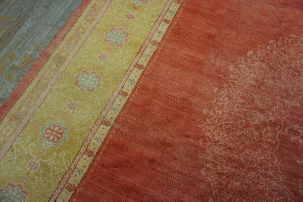 Rust-colored rug with a wide lime-green border featuring floral medallions rests on distressed plank flooring.