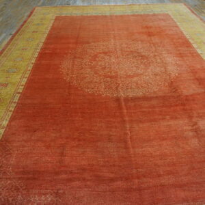 Orange rug with a faded medallion, yellow patterned border, lying on worn wooden planks.