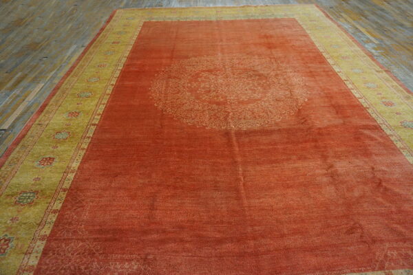 Orange rug with a faded medallion, yellow patterned border, lying on worn wooden planks.