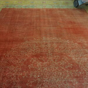 Red rug with faded medallion and vibrant green patterned border, resting on wood floor.