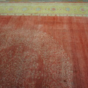 Low pile distressed red rug showing a faded central design and a contrasting yellow floral border.