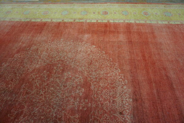 Low pile distressed red rug showing a faded central design and a contrasting yellow floral border.