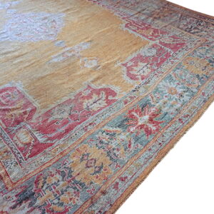 Traditional ornate rug with a faded yellow center and borders detailed in red, muted teal, and gray.