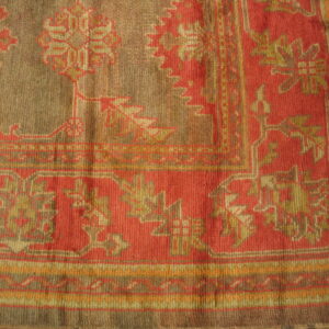 Close corner view of a low-pile rug featuring stylized patterns in terracotta red, taupe, and gold.