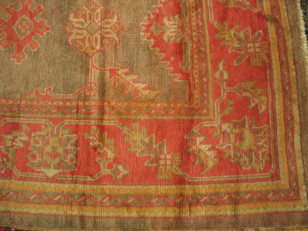 Close corner view of a low-pile rug featuring stylized patterns in terracotta red, taupe, and gold.