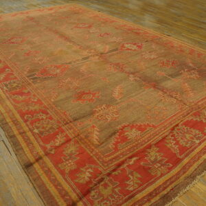 Brown-tan rug with red and gold geometric patterns and a wide border rests on worn wooden floorboards.