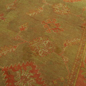 Low-pile textured rug in muted olive and orange with distressed traditional floral patterns and border.