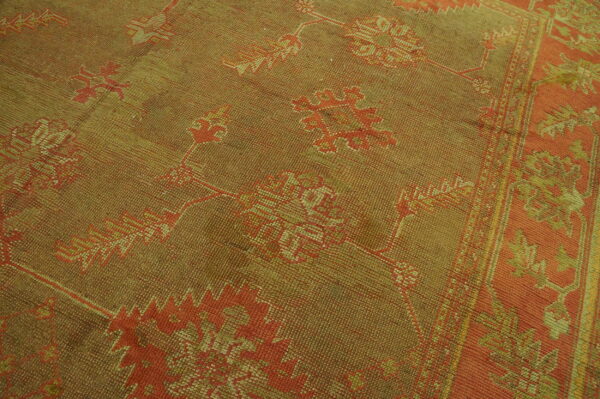Low-pile textured rug in muted olive and orange with distressed traditional floral patterns and border.
