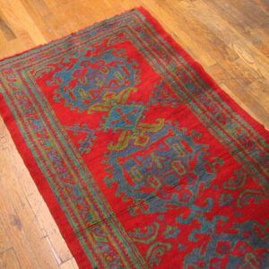 Red runner rug featuring teal and olive traditional motifs on a distressed hardwood floor.
