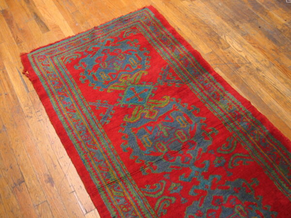 Red runner rug featuring teal and olive traditional motifs on a distressed hardwood floor.