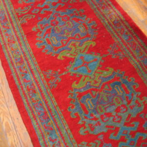 Bright red runner rug with bold turquoise, slate blue, and lime green geometric patterns on wood flooring.