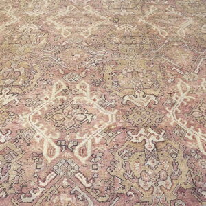 Detailed, low-pile rug featuring ornate diamond and floral patterns in faded rose, beige, and cream.