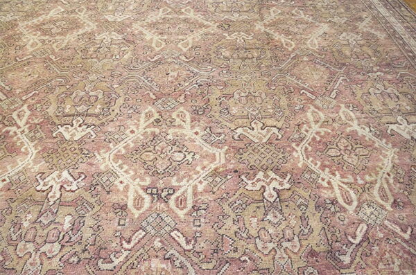Detailed, low-pile rug featuring ornate diamond and floral patterns in faded rose, beige, and cream.