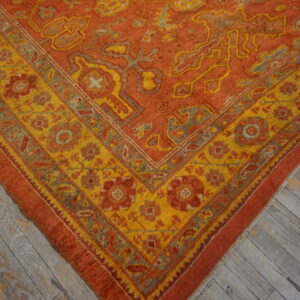 Textured orange and yellow rug corner showing floral medallions, placed on weathered grey plank flooring.