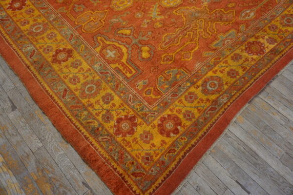 Textured orange and yellow rug corner showing floral medallions, placed on weathered grey plank flooring.