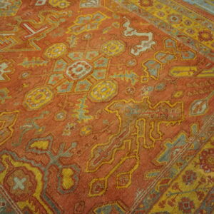 Terracotta rug with complex yellow and slate blue traditional geometric motifs on gray distressed wood flooring.