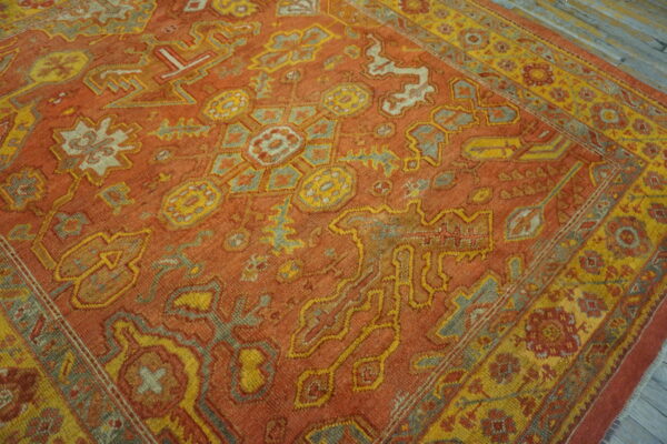 Terracotta rug with complex yellow and slate blue traditional geometric motifs on gray distressed wood flooring.