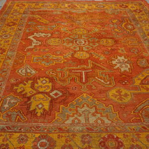 Traditional orange rug with complex gold and taupe geometric patterns rests on old wood planks.