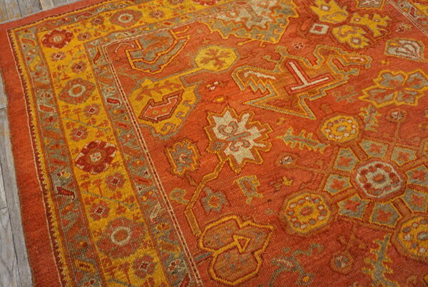 Geometric rug in rust, yellow, and gray with stylized floral patterns on a gray wood floor.