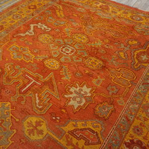 Geometric patterned rust rug with gold and gray accents borders sits on distressed gray wood planks.