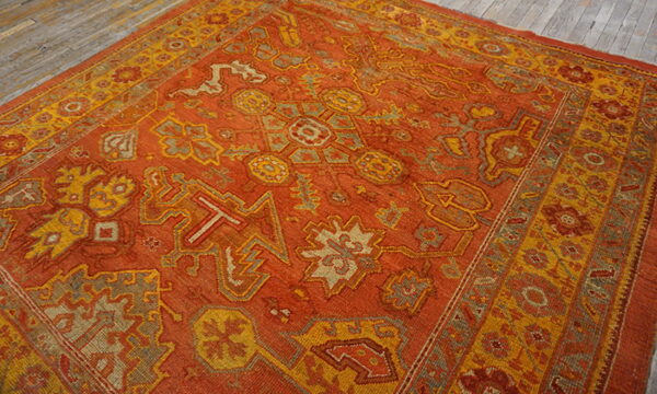 Geometric patterned rust rug with gold and gray accents borders sits on distressed gray wood planks.