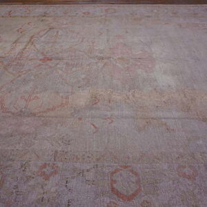 A large, faded low-pile rug features muted gray and pink abstract traditional patterns on a wooden floor.