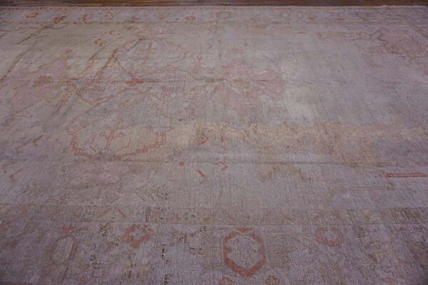 A large, faded low-pile rug features muted gray and pink abstract traditional patterns on a wooden floor.