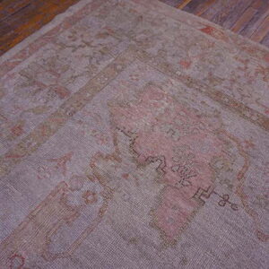 Faded mauve and coral patterned rug with low pile texture lying on rustic dark hardwood flooring.