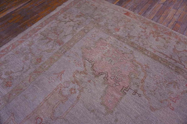 Faded mauve and coral patterned rug with low pile texture lying on rustic dark hardwood flooring.