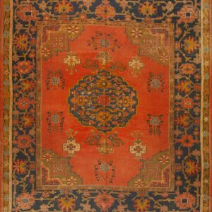 Ornate traditional rug with a coral field, stylized floral motifs, and wide indigo borders.