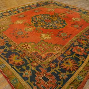 Traditional square rug with coral red, navy, and green geometric and floral patterns on wooden flooring.