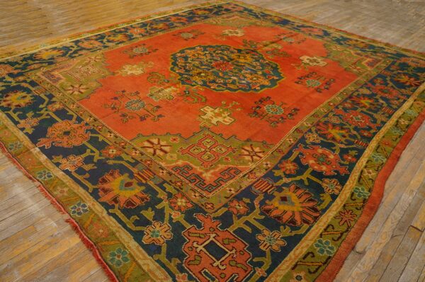 Traditional square rug with coral red, navy, and green geometric and floral patterns on wooden flooring.